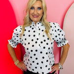 Black and white polka dot blouse with puff sleeves, ruffle neckline, and button-front detail.