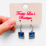 Faceted blue square crystal drop earrings suspended from polished silver-tone hoops.