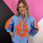 Light blue top with orange scroll print, ruffled neckline, and puff sleeves.