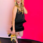 Side profile of the black feather cami paired with a purse, highlighting the feather trim, sleeveless fit, and flattering silhouette.