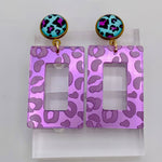 Purple mirror acrylic rectangle earrings with teal and magenta leopard-print stud.