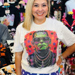 Cream tee with colorful Frankenstein, oversized sunglasses, layered necklaces, rhinestones, and polka dots.