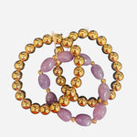 Three-piece gold and lavender beaded bracelet stack with water-resistant design.