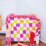 Checkerboard quilted bag with floral ruffle trim and zipper closure.