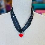 A black scarf necklace with delicate white patterns, accented by a bold red heart charm for a striking contrast. A lightweight, stylish piece perfect for adding a pop of personality to any outfit.