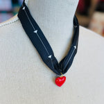 A black scarf necklace with delicate white patterns, accented by a bold red heart charm for a striking contrast. A lightweight, stylish piece perfect for adding a pop of personality to any outfit.