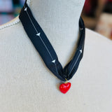A black scarf necklace with delicate white patterns, accented by a bold red heart charm for a striking contrast. A lightweight, stylish piece perfect for adding a pop of personality to any outfit.