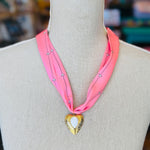 Close-up of a pink printed scarf-style necklace featuring a gold heart charm with a smooth white stone center, styled on a white background for a soft and elegant presentation.