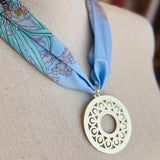 Blue printed scarf necklace with the words “lovely tiger,” featuring a gold cutout medallion charm; a playful and whimsical accessory perfect for adding a touch of charm and elegance to any outfit.