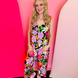 Black floral jumpsuit with shoulder ties, scalloped wide-leg hems, and vibrant multicolor blooms.