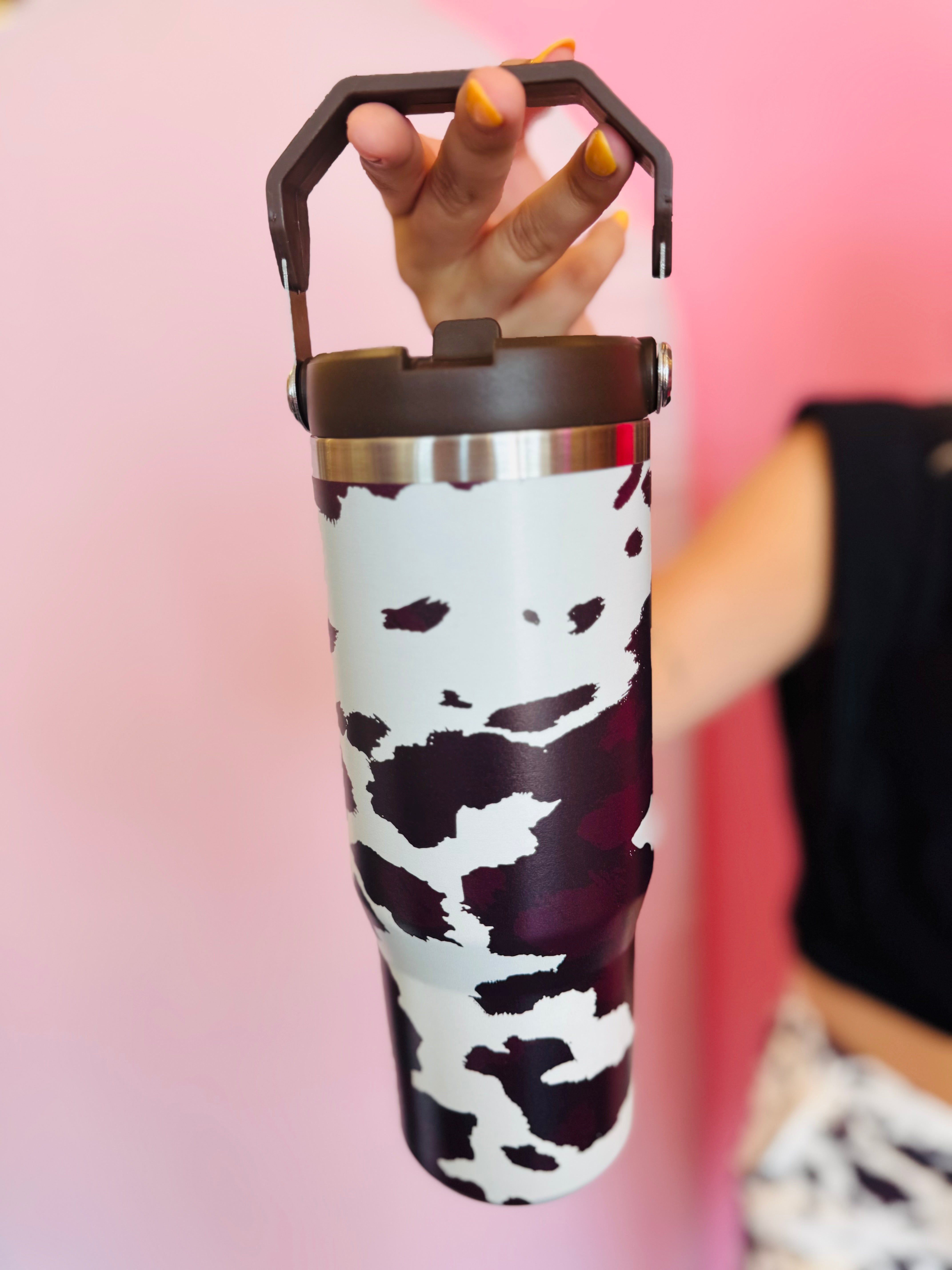 Chocolate cow print insulated tumbler with handle, screw-on lid, and car cup holder–friendly base.