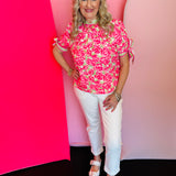 Bright pink floral top with green accents, striped neckline trim, and short sleeves with adjustable ties