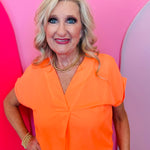 Neon orange woven blouse with V-neckline and cuffed short sleeves.