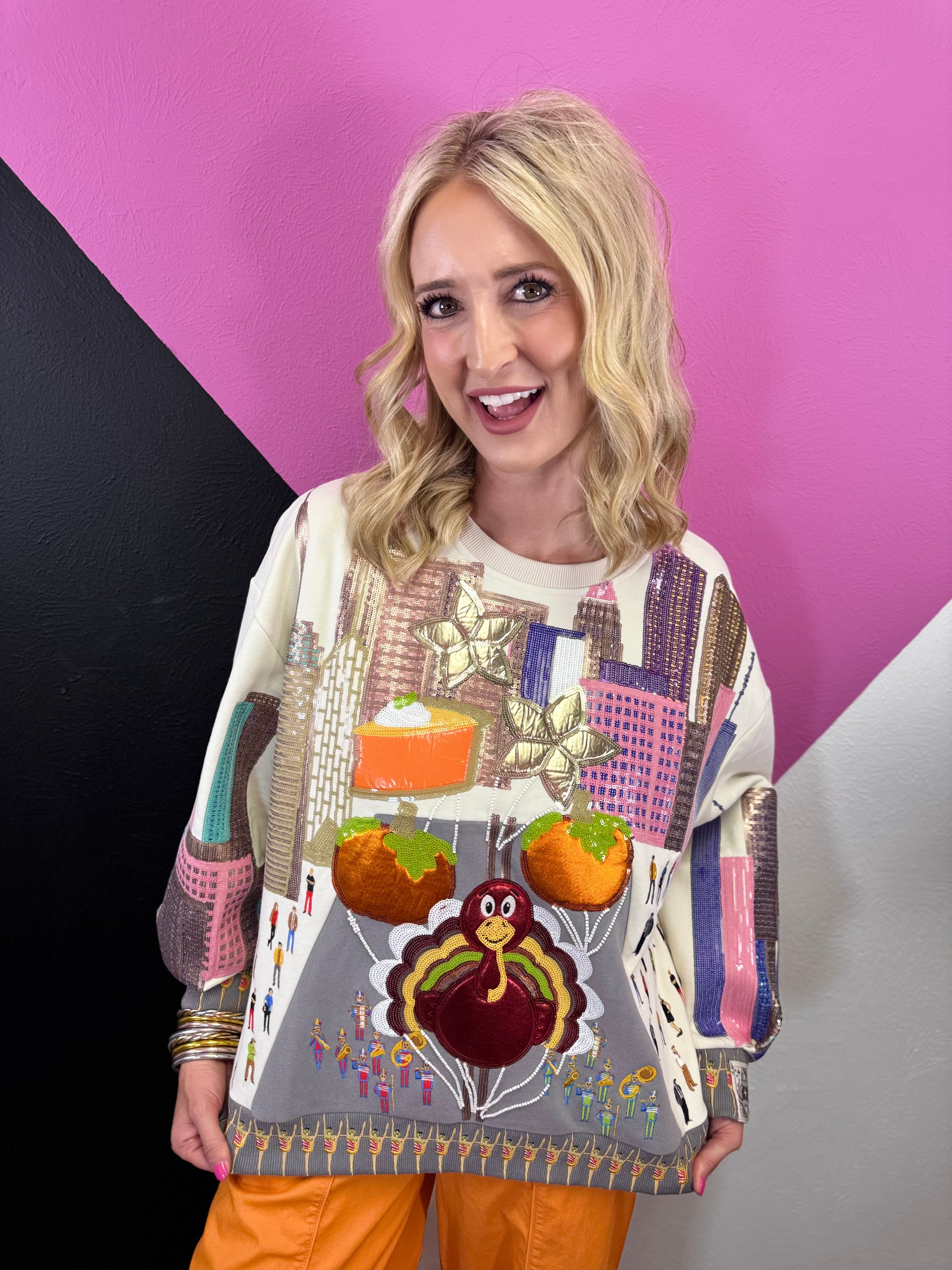 Colorful Thanksgiving parade sweatshirt with festive floats, pumpkins, city details, and turkey centerpiece.