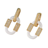 White enamel oval earrings with gold rhinestone hoops and geometric design.