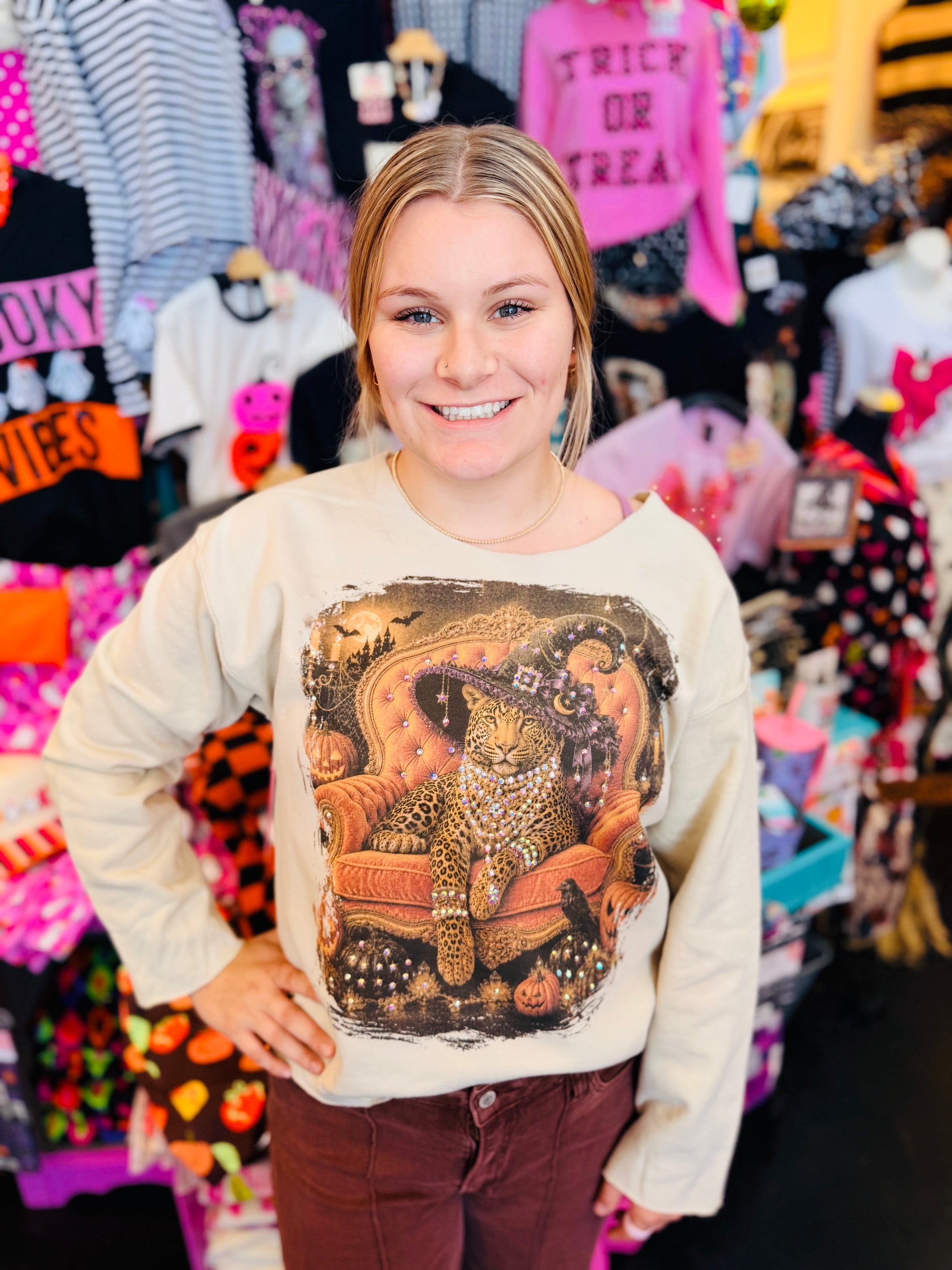 Cream sweatshirt with jeweled leopard in witch hat, orange chair, pumpkins, bats, and spooky accents.