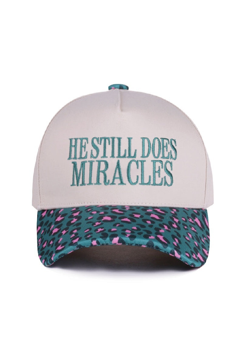Zenana White cap with turquoise “He Still Does Miracles” embroidery and cougar-print bill, adjustable fit.
