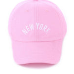 Pink cotton baseball cap with white embroidered “New York” and adjustable brass buckle closure.
