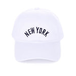 White cotton baseball cap with black embroidered “New York” and adjustable brass buckle closure.