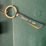 Keychain with 'FUCK IT UP' tag on a green textured surface