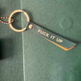 Keychain with 'FUCK IT UP' tag on a green textured surface
